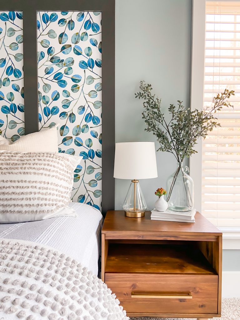 Wallpapered faux headboard with colorful printed wallpaper and warm wood side table.