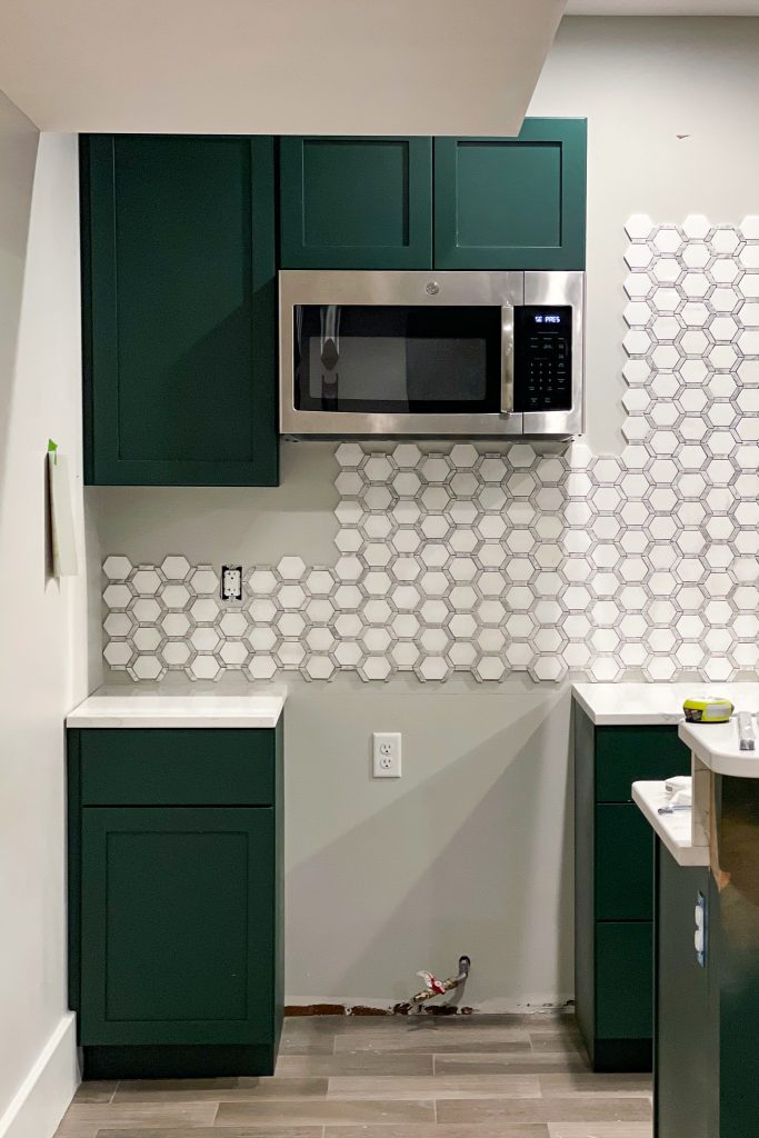 the kitchen wall partially tiled with Jeffrey Court Norton Mosaic, dark green cabinets | HauteHouseLove.com