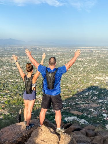 woman and man on the top of a mountain looking over a city with their arms raised above their heads | found on HauteHouseLove.com